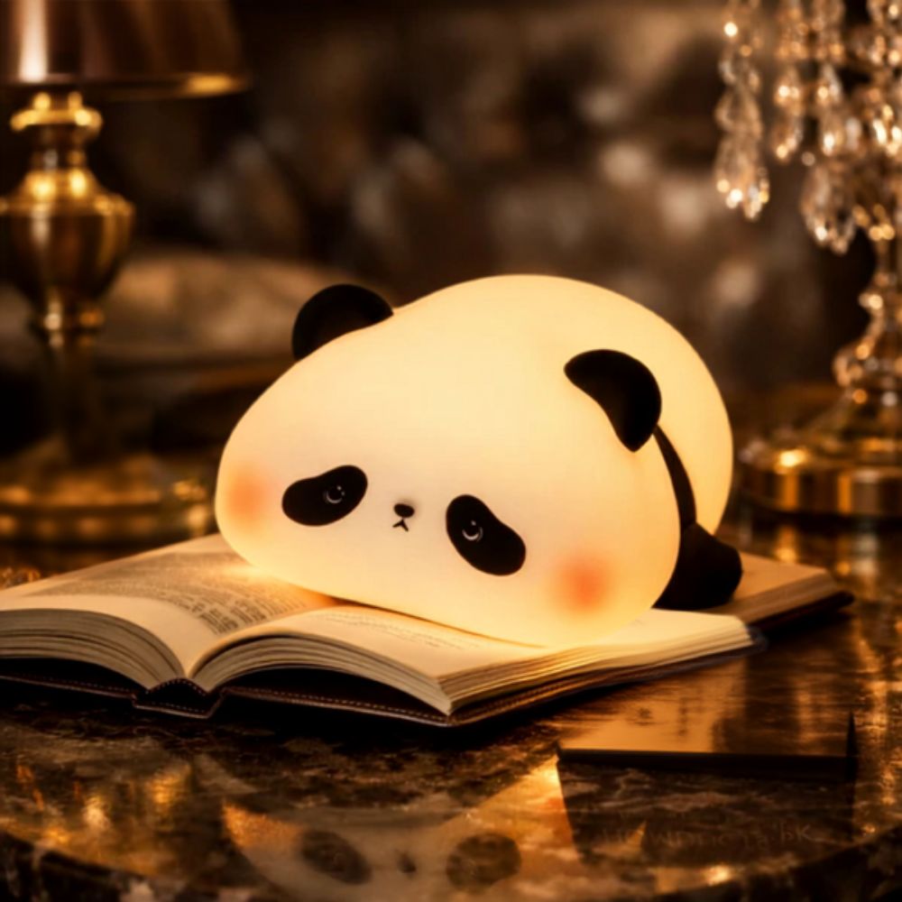 A cute, glowing panda-shaped night light resting on an open book on a polished dark table, with warm ambient background lighting.