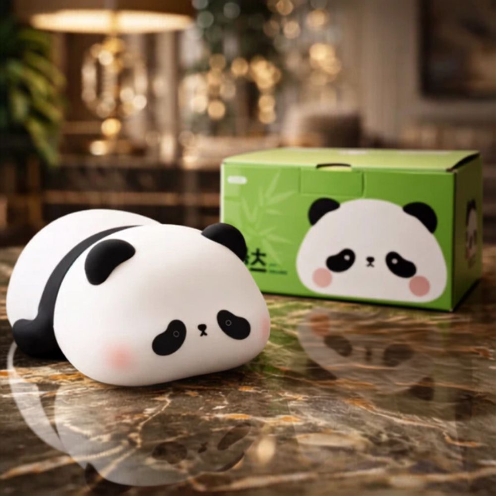 A cute, squishy panda-shaped object with a black-and-white face and pink cheeks sits on a polished marble surface, with its green printed box behind it in a softly blurred indoor setting.
